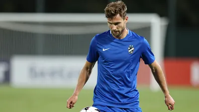 A mid-30s anonymous Häcken player in a tight waist-up shot, wearing a solid blue kit, focused on the ball, background...