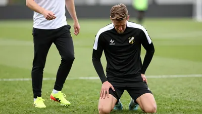 A 25-year-old Häcken midfielder in a black and white training top, his face etched with frustration, kneels on the...