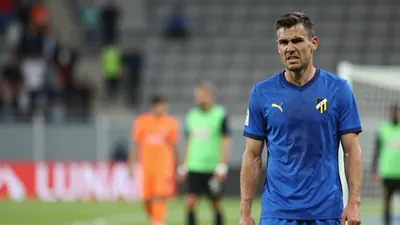 A Häcken player in a blue jersey with a crest on the chest, mid-action during a match, looking frustrated as he stands...