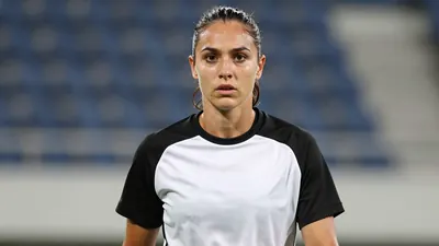 Mid-20s female striker, athletic build, waist-up, intense gaze, hair pulled back, wearing a plain black and white...